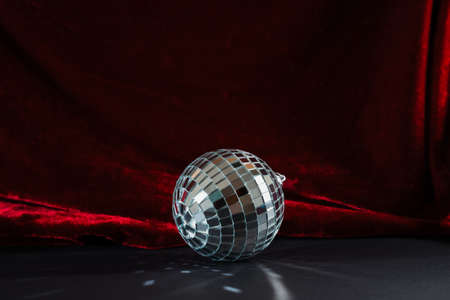 silver mirror disco ball on black paper and red velvet curtain background. Holiday season Christmas and New Year retro party with copy spaceの写真素材
