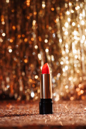 red lipstick in silver and black tube on rose gold sequin and silver tinsel lametta background. Self care and beauty for the christmas new year holiday seasonの写真素材