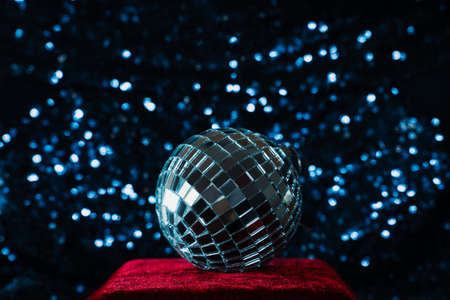 silver disco ball on red velvet podium on blue sequin background. Holiday season Christmas and New Year retro party with copy spaceの写真素材