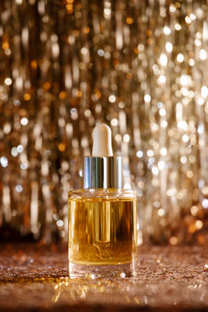 face oil in glass bottle with silver cap and dropper on rose gold sequin and silver tinsel lametta background. Self care and beauty for the christmas new year holiday seasonの写真素材