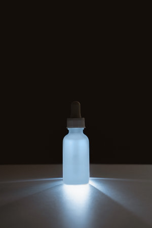 backlit face serum in white matte glass bottle with dropper on dark background. Anti aging facial liquid with peptides and collagenの写真素材