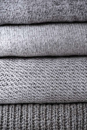 stack of warm grey knit sweaters on white table and gray background. Cold autumn season texture detailの写真素材