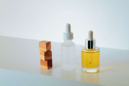 Face serum in matte glass bottle and face oil and stacked wood cedar cubes on white background. Building your skin-care routine regimen with peptides and collagenの写真素材