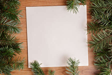dark green lush pine fir branch frame on light brown wood and recycled white paper background fir leaves. Christmas tree or holiday card design for eco-friendly natural products or cottage bannerの写真素材