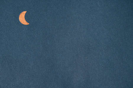 Orange metal crescent moon on navy blue kraft paper. Textured background with geometric shapes