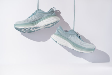 Strasbourg, France - August 2023 : Hoka Bondi 8 new green running shoes on white background suspended from straps. Stylish monochrome shoes for active people that incorporate new health technologyのeditorial素材