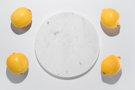 Fresh yellow lemons next to marble circle background on white. Hard light top view. Fresh food and vitamin C in nutrition and skincareの写真素材