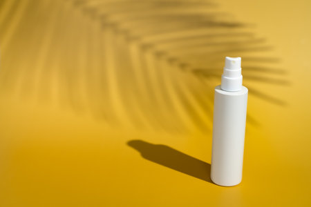 Blank white spray bottle on yellow background in direct sunlight with palm tree shadow. Summer skin...