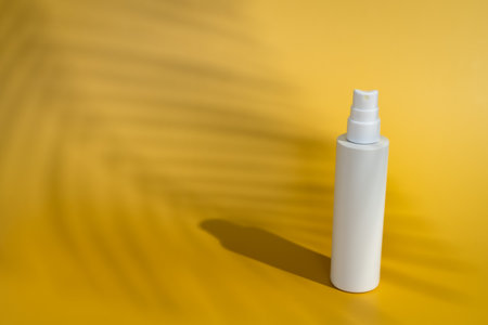 Blank white spray bottle on yellow background in direct sunlight with palm tree shadow. Summer skin...