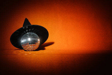 A witch hat and a disco ball on an orange background. Creative Halloween party wallpaperの写真素材