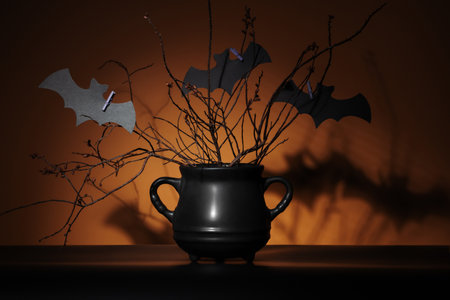 Mysterious black cauldron with dry plants and cutout bats in spotlight on pumpkin orange background. Represents Halloween, crafts, magic, and fantasy concepts.の写真素材