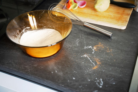 On the kitchen counter, a bowl filled with flour sits prominently beside a whisk, ready for various...