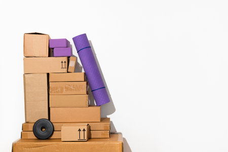 Creative minimalist image of stacked cardboard boxes and sport equipment on a plain background,...