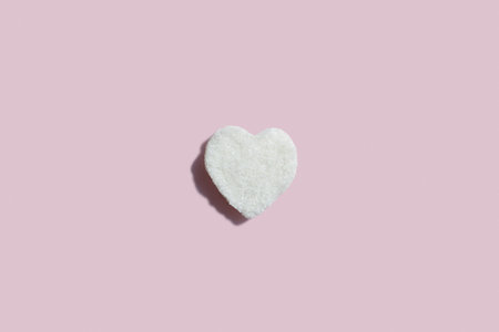 A heart shaped sugar cube sits against a pastel pink backdrop, symbolizing sweetness, love, and simplicity in minimalist design. Perfect for romantic, culinary, or creative concept themes.の写真素材