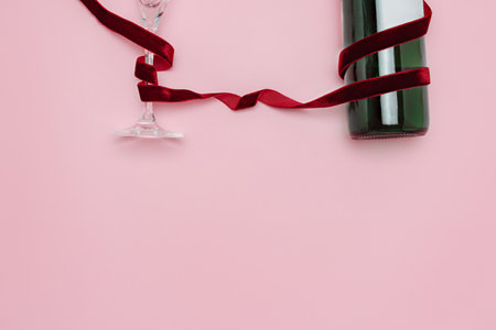 A minimalist and creative composition featuring a wine bottle, glass, red velvet ribbon on a soft pink background, representing elegance, celebration, and sophisticated design.の写真素材