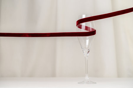 A minimalist and creative composition featuring a wine glass, red velvet ribbon on a soft cream background, representing elegance, Valentines celebration, and sophisticated design.の写真素材