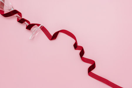 A minimalist and creative composition featuring a wine glass, red velvet ribbon on a soft pink background, representing elegance, Valentines celebration, and sophisticated design.の写真素材