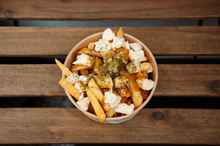Poutine fries with cheeses and sauce in paper takeout container. Delicious freshly prepared meal,...