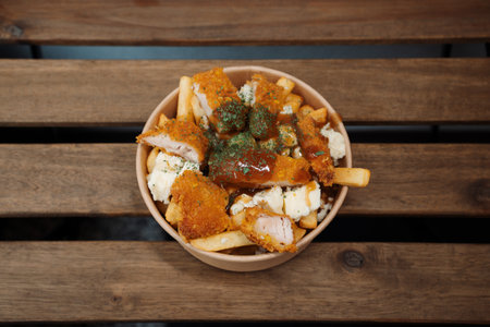 Poutine fries with chees and fried chicken in paper takeout container. Delicious freshly prepared...