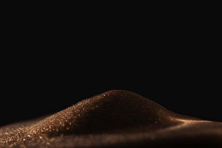 Gold sparkly hourglass sand on black background. Minimalist low key poto for concepts of time, travel to the desertの写真素材