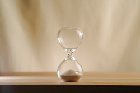 A simple hourglass on a wooden table with a beige backdrop, symbolizing time flow and minimalistic living. Represents timeless themes in a creative, uncluttered presentation for stylish concepts.の写真素材
