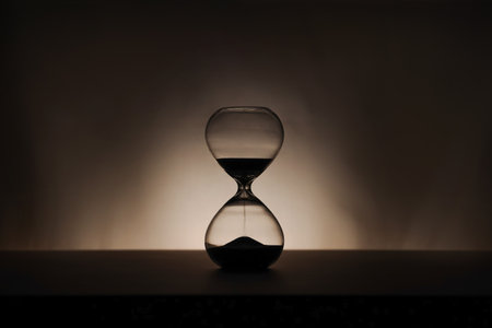 A simple hourglass on a wooden table with a beige backdrop, symbolizing time flow and minimalistic...