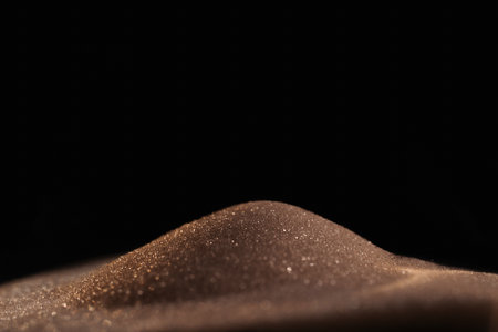 Gold sparkly hourglass sand on black background. Minimalist low key photo for concepts of time,...
