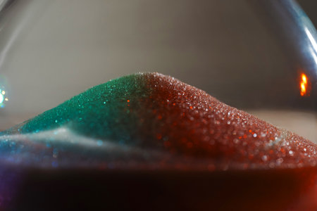 Rainbow sparkly hourglass sand on light background. Minimalist low key for concepts of time, travel...