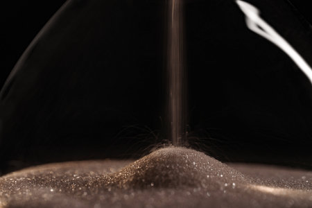 Gold sparkly hourglass sand on black background. Minimalist low key poto for concepts of time,...