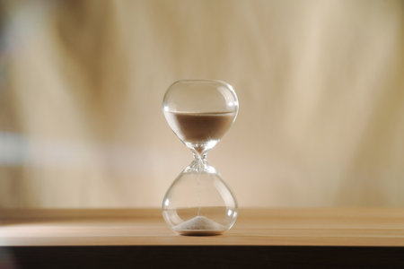 A simple hourglass on a wooden table with a beige backdrop, symbolizing time flow and minimalistic living. Represents timeless themes in a creative, uncluttered presentation for stylish concepts.の写真素材