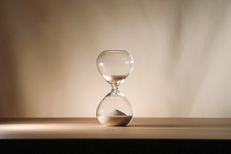 A simple hourglass on a wooden table with a beige backdrop, symbolizing time flow and minimalistic...