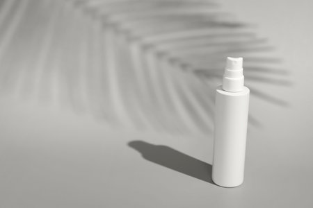 Blank spray bottle on background in direct sunlight with palm tree shadow. Summer skin protection mockup template with minimalist beach aesthetic color of 2026 year cloud whiteの写真素材