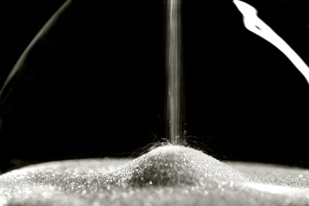 Sparkly hourglass sand on black background. Minimalist low key photo for concepts of time, travel to...