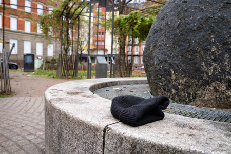 Black knitted hat resting on the edge of a fountain in a city square. Everyday urban scene showing a...