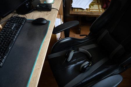 PC desk with gamer headphones resting on an old gaming chair in a casual home setup. Everyday...
