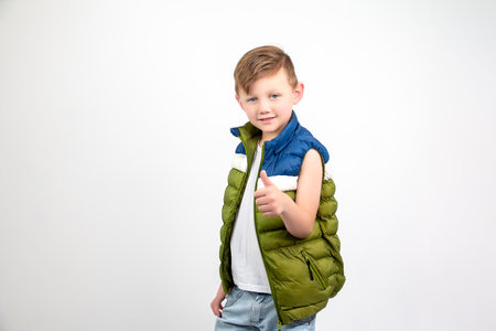 Blonde boy with blue eyes in white t-shirt, green, blue and white vest and jeans, posing for the photo.の写真素材