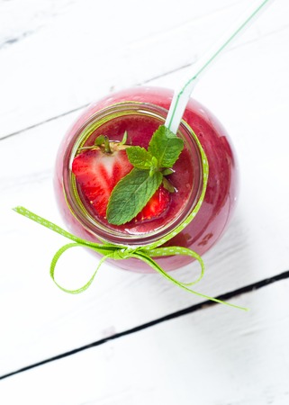 Strawberry smoothie in a glass jar with green ribbon at the white tableの写真素材
