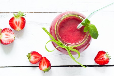 Strawberry smoothie in a glass jar with green ribbon at the white table with fresh berriesの写真素材