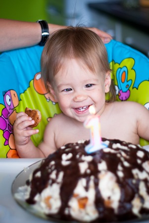 Baby boy blows out candles on a cake on his first birthday