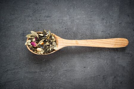 Green Sencha tea flavored with flowers and zest in a wooden spoon on a dark backgroundの写真素材