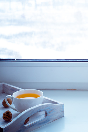 A cup of hot tea in white cup on the windowsill in the winter frosty day.の写真素材