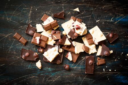 Different varieties of chocolate. White chocolate with hazelnuts and cranberries, milk and dark chocolate with hazelnuts on the dark table.の写真素材