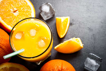 Fresh orange juice, orange slices, mint leaves and ice on dark background. Top view with copy space.の写真素材