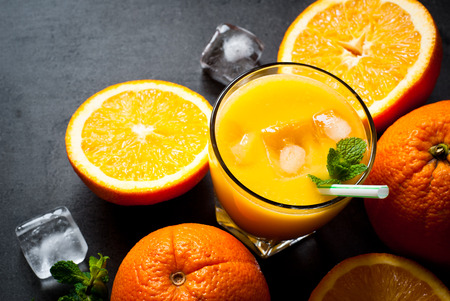 Fresh orange juice, orange slices, mint leaves and ice on dark background. Top view with copy space.の写真素材