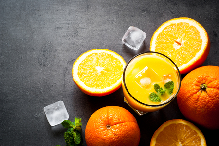 Fresh orange juice, orange slices, mint leaves and ice on dark background. Top view with copy space.の写真素材