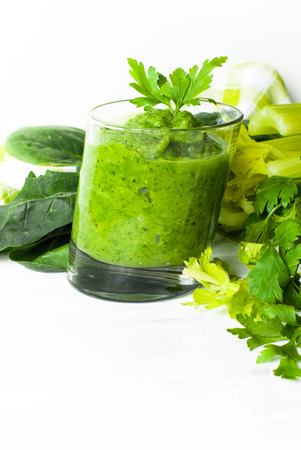 Green vegetable smoothie with celery, spinach and herbs in a asymmetrical glass on a white. Space for text. Healthy food concept.の写真素材
