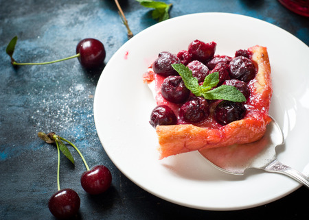 Homemade cherry pie with sugar powder on blue table. View from above.