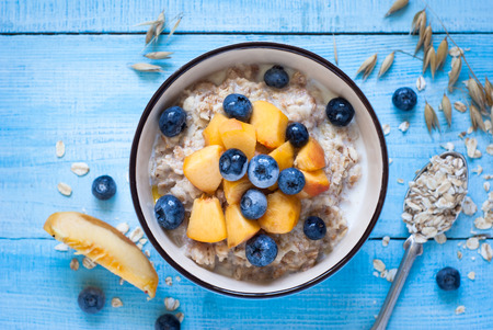 Oatmeal with peach and blueberries at blue wooden table. Flat lay.の写真素材