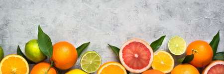 Different citrus fruit on grey concrete table. Whole and sliced fruit. Food background. Healthy...