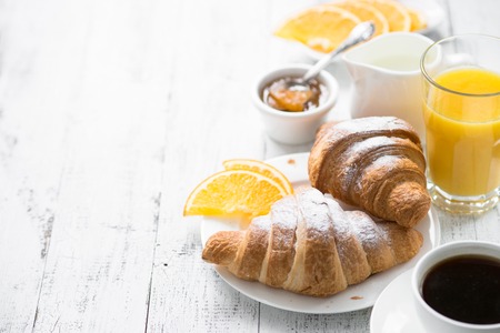 Croissant jam coffee orange jice at white wooden table.